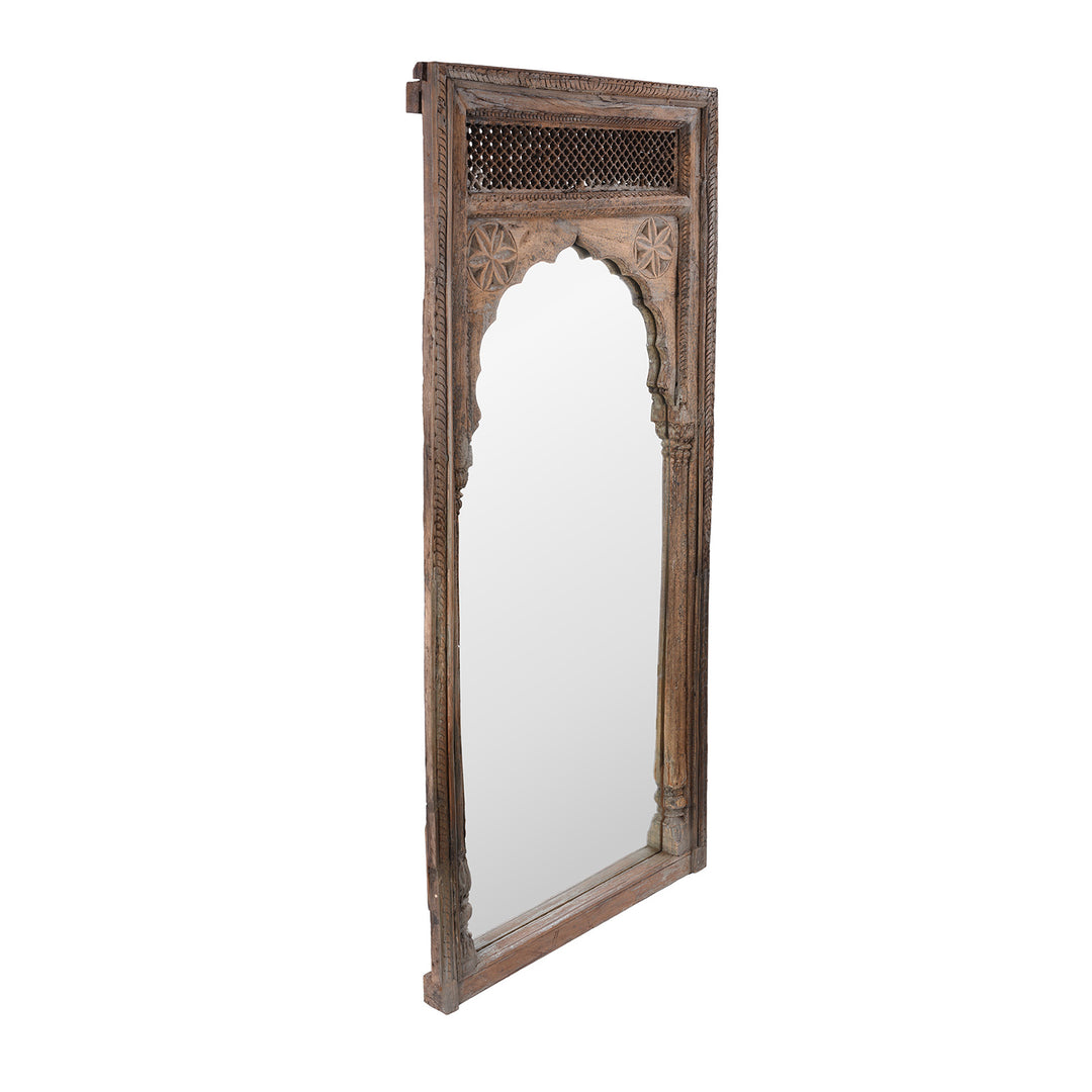 Angled View Of  Antique Indian Teak Window Mirror With Arched Frame And Intricate Lattice Carving At The Top
