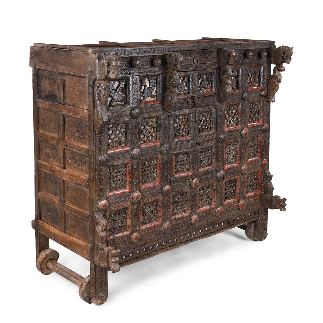 Angled VIew Of Antique 19th-century Indian dowry chest from Gujarat with intricate animal carvings, geometric patterns, and hidden compartments, set on wheels.