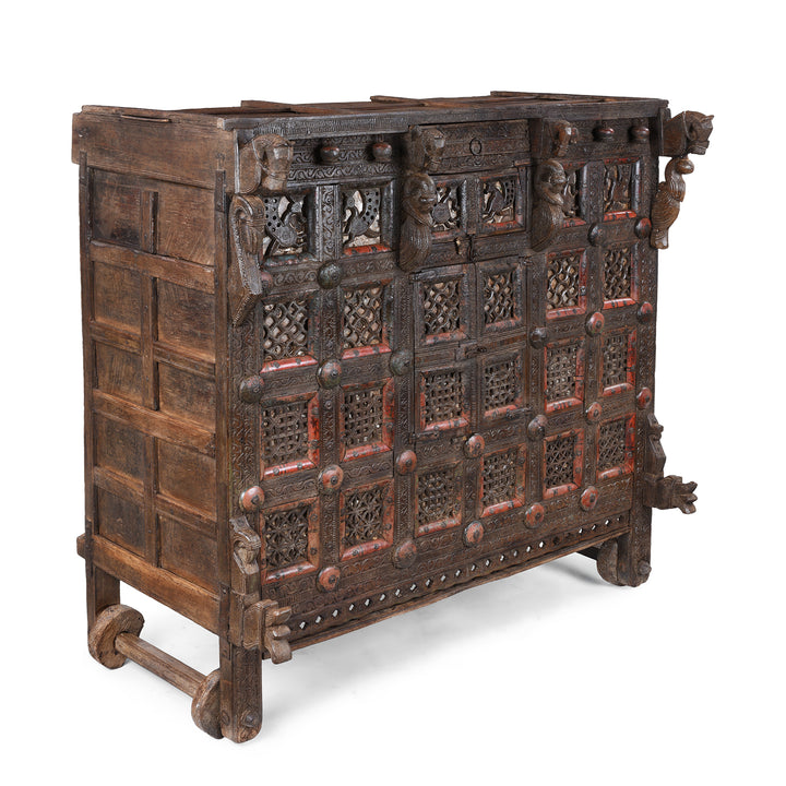 Angled VIew Of Antique 19th-century Indian dowry chest from Gujarat with intricate animal carvings, geometric patterns, and hidden compartments, set on wheels.