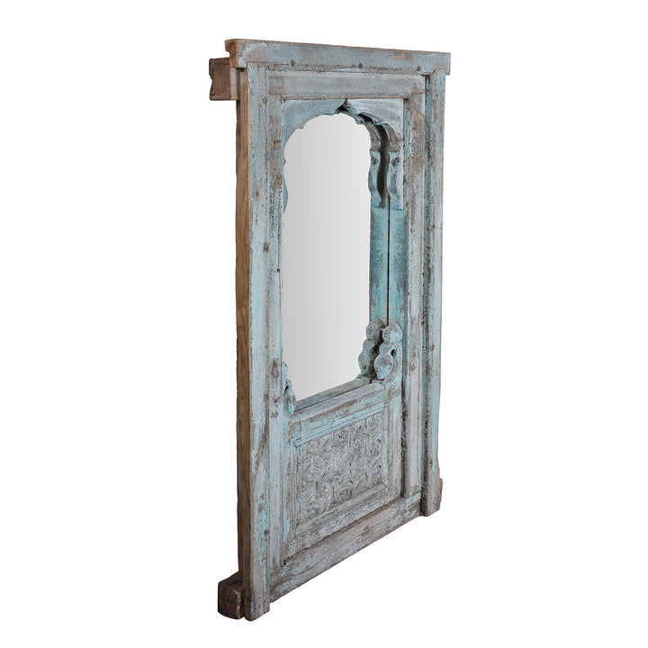 Angled View Of Antique Indian Teak Mirror With Mughal Arch And Carved Base Panel In Distressed Blue Paint
