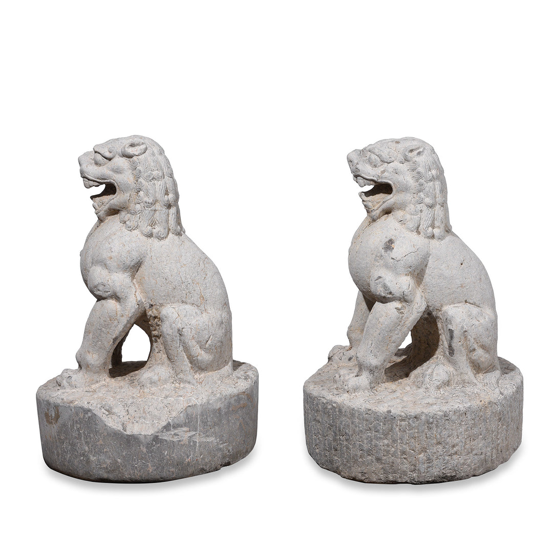 Side View Of Pair Of Carved Stone Chinese Guardian Lions With Stylised Manes Seated On Circular Plinths