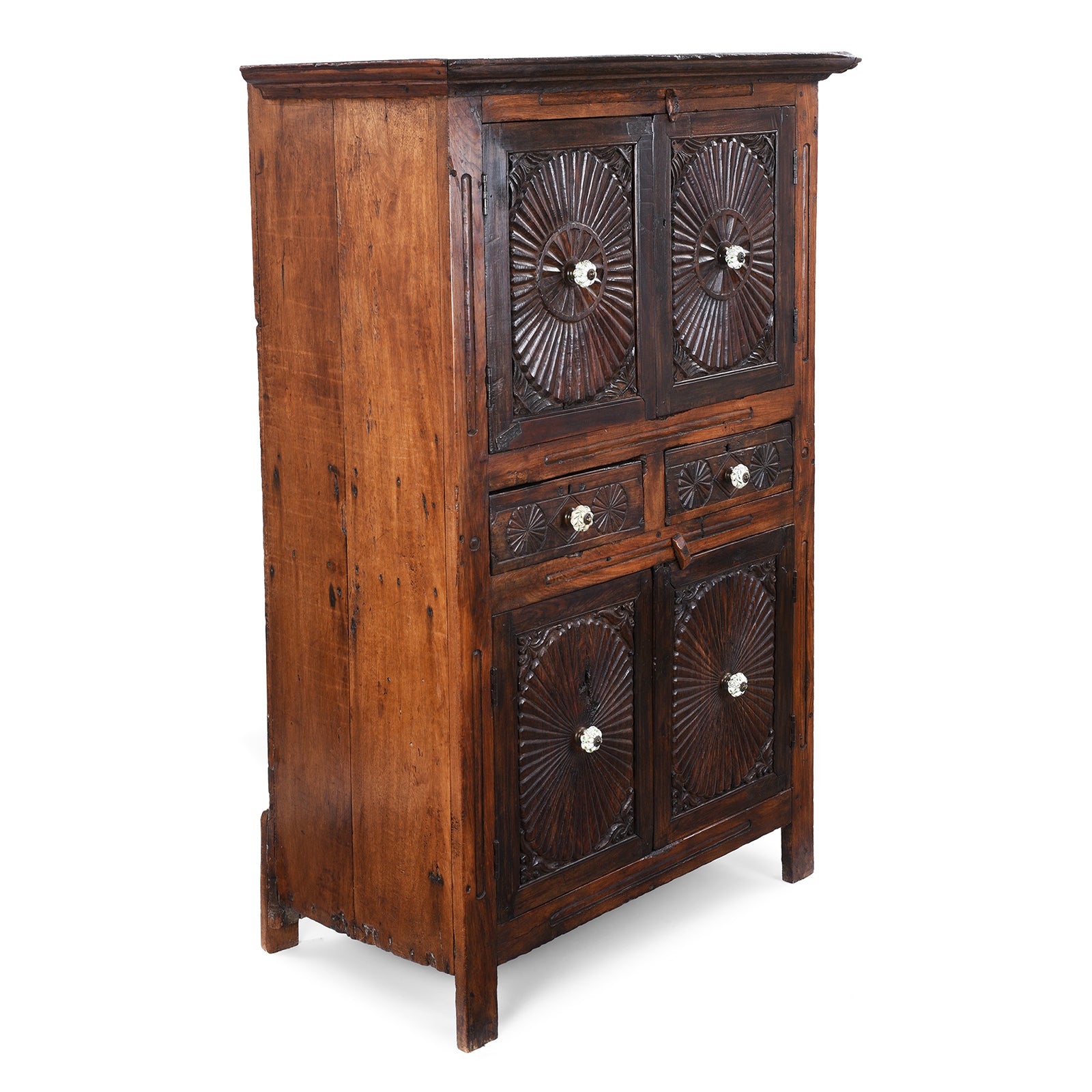 Angled View Of Indian Teak Almirah Cabinet With Hand-Carved Sunburst Panels, Two Drawers And White Ceramic Handles