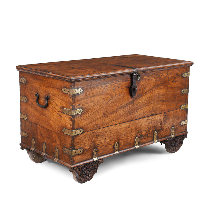 Angled View Of Antique mid-19th century teak chest from Gujarat with hidden wheels, carved floral feet, and original iron fittings.