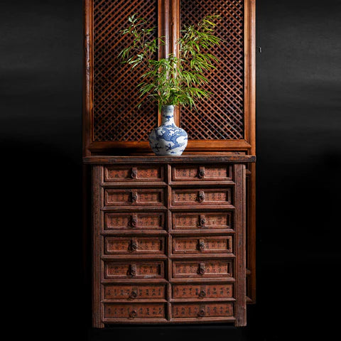 A dark wood Chinese cabinet in front of a wooden screen and black wall