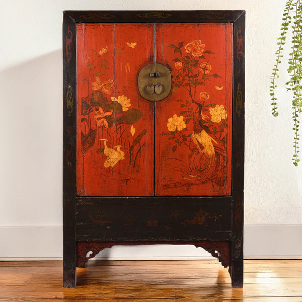 A red Chinese cabinet with flower details next to a house plant