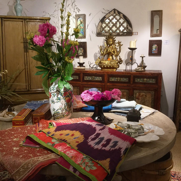 An Indian painted fanlight mirror with an antique Mongolian sideboard with a bronze Tibetan Tara statue sitting atop and an olive green lacquer tapered cabinet from China