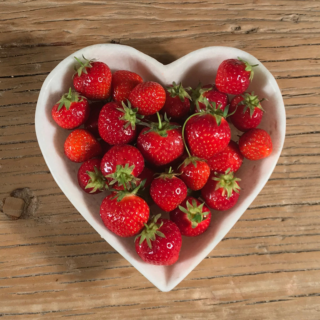 A mughal style white marble heart shaped bowl handmade in India filled with strawberries